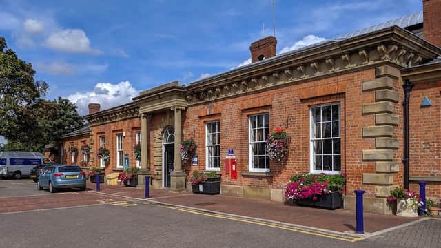 Brick building with large windows, flower planters, a red post box, and parked cars under a blue sky.