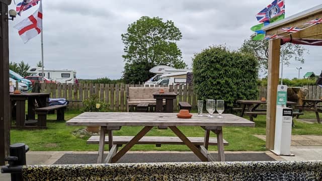 Outdoor seating area at The Providence Inn with picnic tables, flags, and a view of caravans and greenery.