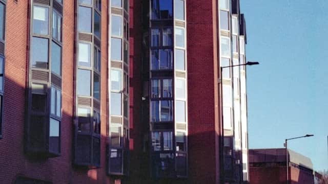 Modern brick building with large windows, reflecting sunlight, alongside parked cars on a city street.