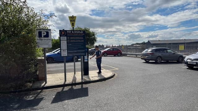 Pay and display parking sign with a person near cars and a cloudy sky in Carlisle Street Car Park, York.