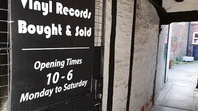 Sign for Earworm Records with vinyl records listed, opening times, and a narrow pathway leading to the shop.