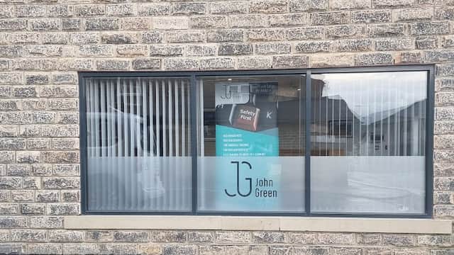 Window display featuring "John Green Health And Safety" signage on a stone building in Cross Hills, Yorkshire.