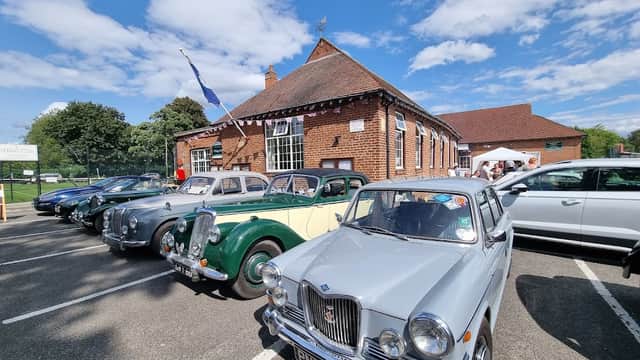 Sutton Upon Derwent Village Hall with classic cars parked in front under a blue sky with scattered clouds.