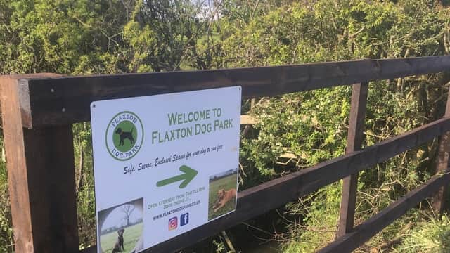 Welcome sign for Flaxton Dog Park on a wooden fence, surrounded by greenery and a view of the park beyond.