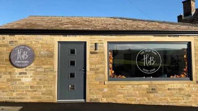 The Hair Barn features a stone exterior, large windows with circular signs, and a modern door under a clear blue sky.