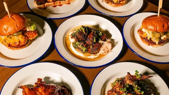A spread of various dishes including poutine, burgers, and chicken wings on white plates against a brown table.