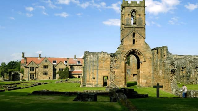 Ruins of Mount Grace Priory with a stone tower, grassy areas, and remnants of walls under a blue sky.