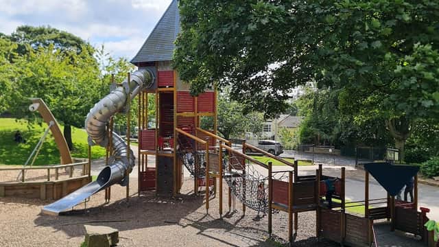 Playground equipment featuring a slide, climbing net, and a tower, surrounded by greenery and trees in Greenhead Park.