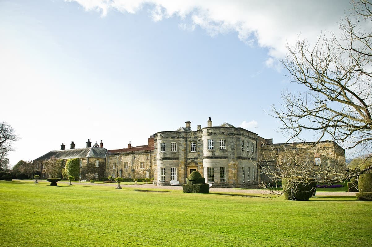 Historic Newburgh Priory with manicured lawns and topiary, set against a clear sky in Coxwold, Yorkshire.