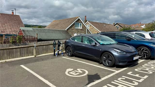 Connected Kerb Charging Station with a parked electric vehicle in a parking lot, surrounded by houses and cloudy skies.