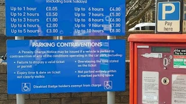 Blue sign detailing parking charges and regulations at Railway Street Car Park, Dewsbury, with a payment machine nearby.