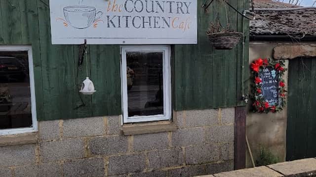 The Country Kitchen Café sign on a green wooden building with a flower pot and seasonal decorations nearby.