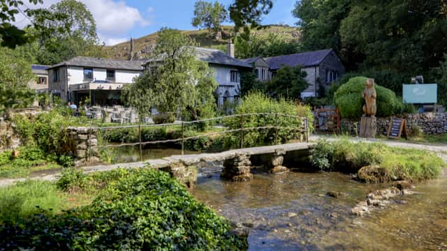 Charming stone cafe with outdoor seating, a small bridge over a stream, and lush greenery in Kirkby Malham, Yorkshire.