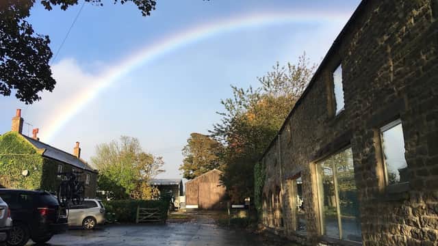 Murk Head Holiday Cottages with a rainbow arching over a stone building and lush greenery in Harwood Dale, Yorkshire.