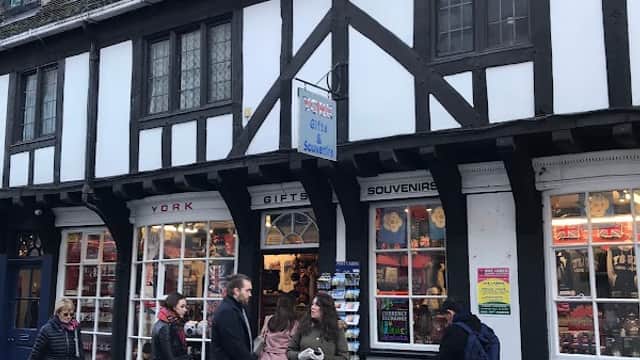 Charming gift shop with Tudor-style architecture, people browsing outside, and colorful souvenirs displayed in windows.