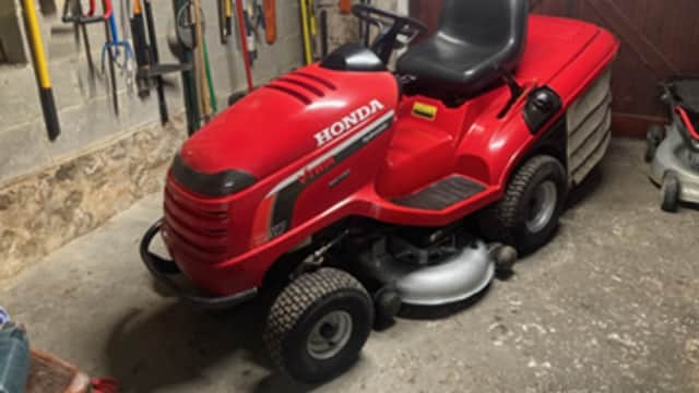 Red Honda lawn mower parked in a garage, surrounded by gardening tools on the wall.