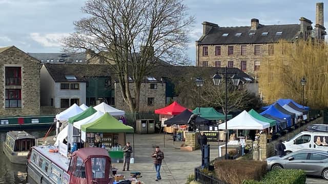 Colorful market tents line the waterfront, with a canal boat and historic buildings in the background.