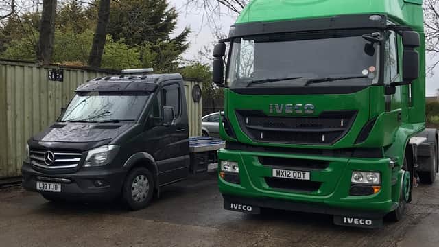 Two commercial vehicles parked side by side: a black Mercedes van and a green Iveco truck in a yard.