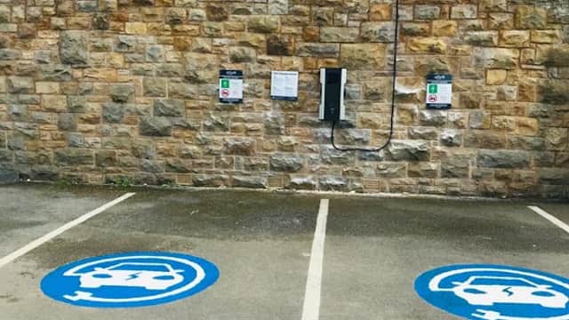 Alfa Power Charging Station with two charging points on a stone wall, marked parking spaces in blue with logos.