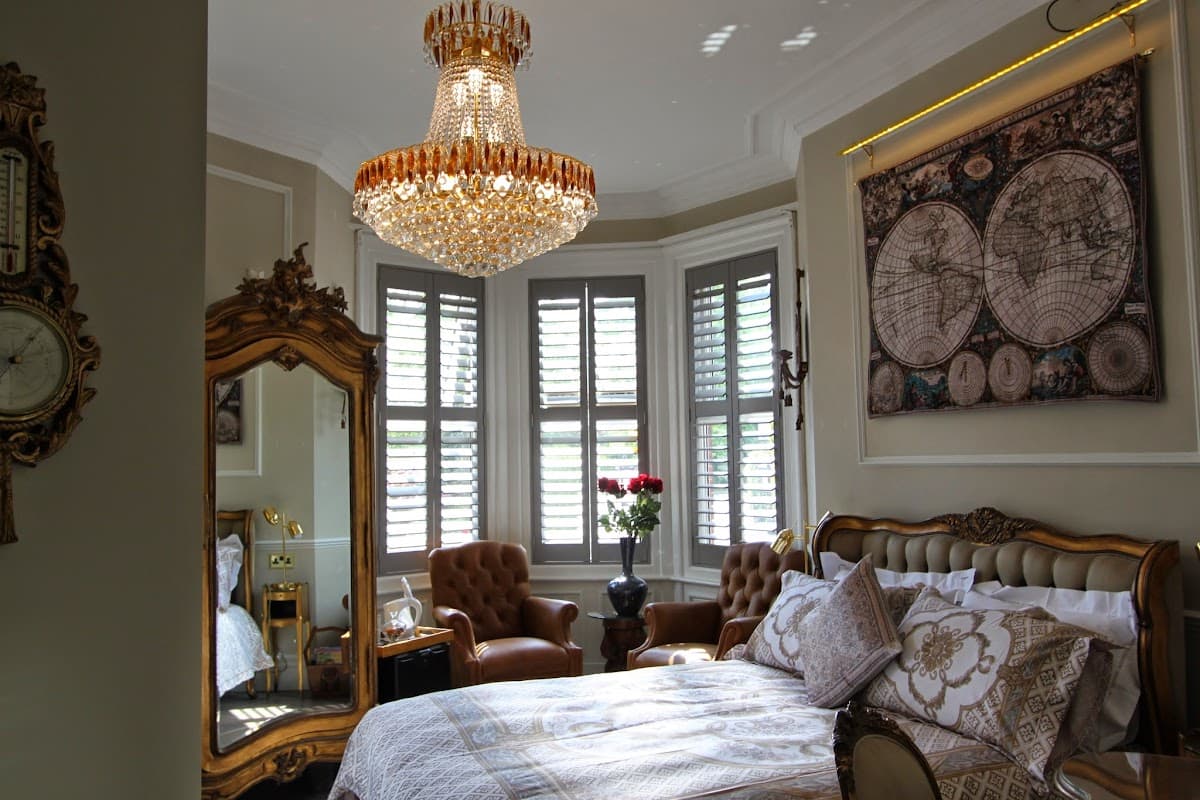 Elegant bedroom featuring a chandelier, vintage mirror, armchairs, and decorative maps on the wall.