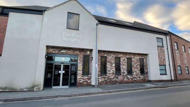 The Park Surgery building with a brick facade, large glass entrance, and cloudy sky in the background.