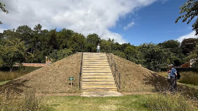 Staircase leading up a grassy mound, surrounded by lush greenery and under a partly cloudy sky.