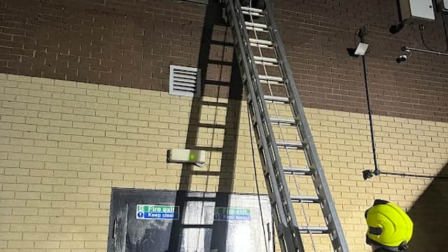 Firefighters using a ladder to assist a person on a balcony at Hillsborough Exchange Car Park at night.