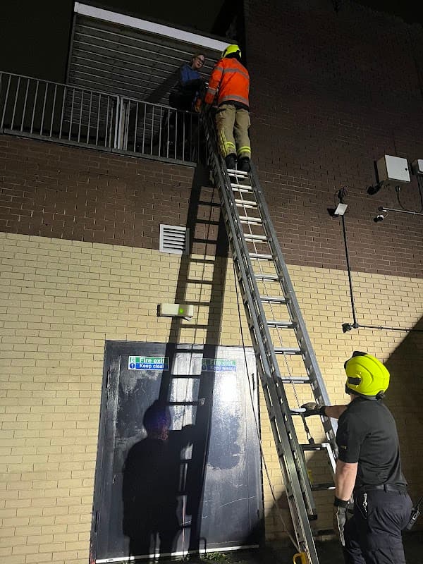 Firefighters using a ladder to assist a person on a balcony at Hillsborough Exchange Car Park at night.