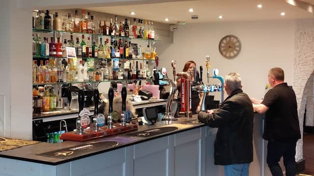 Bar area at The Dacre Arms featuring a variety of spirits, taps, and two patrons engaged in conversation.