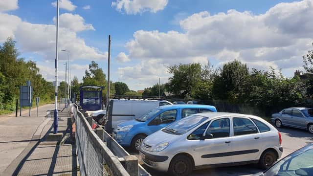 Snaith station car park with several parked cars under a blue sky and fluffy clouds, surrounded by greenery.