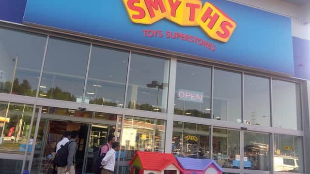 Brightly colored Smyths Toys Superstores sign above entrance, with open doors and a children's playhouse outside.