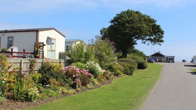 Colorful flower beds line a pathway leading to caravans and a building at Seaside Caravan Park in Skipsea, Yorkshire.