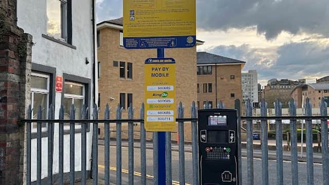 Pay & Display parking sign and payment machine at Bolton Road Car Park, with buildings and a cloudy sky in the background.
