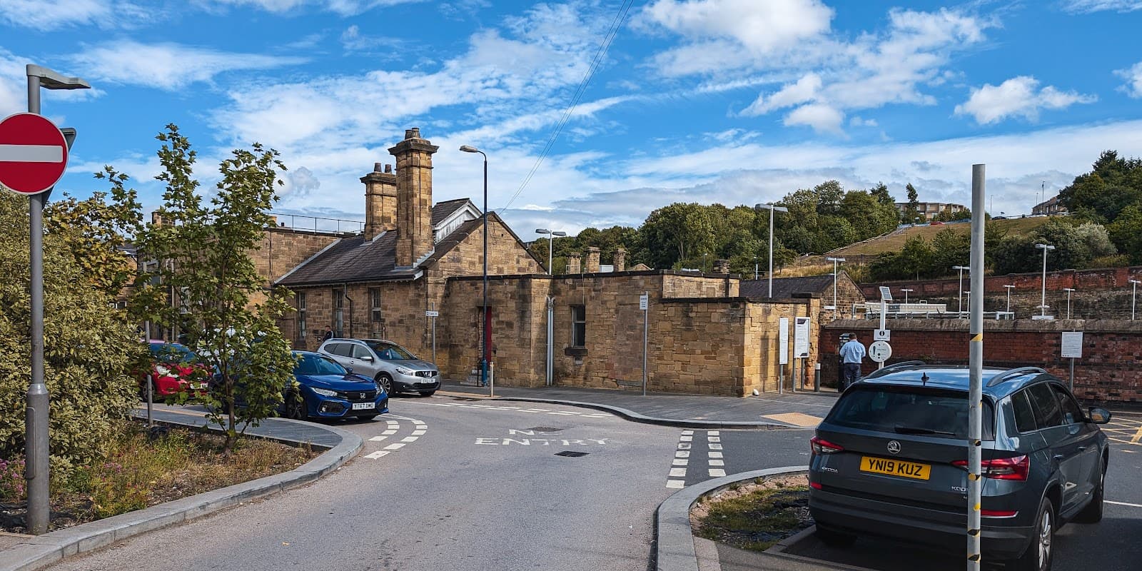 Sheffield Station Short Stay Car Park entrance with stone buildings, parked cars, and a clear blue sky.