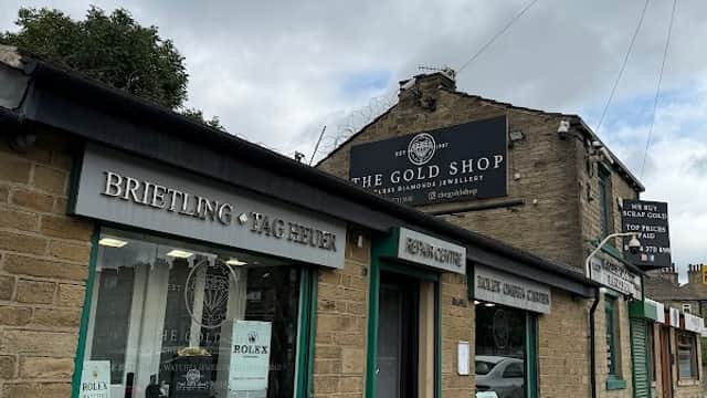 Jewellers storefront with stone facade, large windows displaying watches, and signs for Breitling and Tag Heuer.