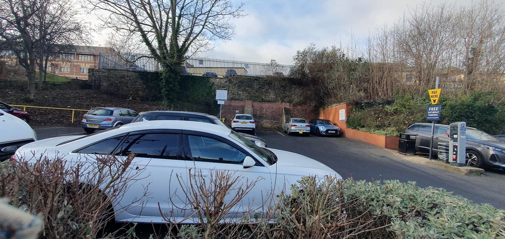 Wellgate North Car Park with parked cars, greenery, and a sign indicating free parking in Rotherham, Yorkshire.