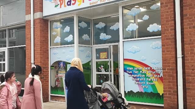 Brightly colored entrance to "The Playground" with children and adults walking by, featuring a rainbow and clouds in the design.