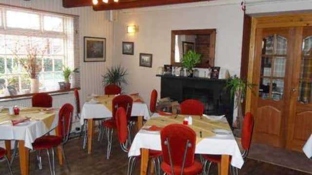 Cozy bar interior with red chairs, white tables, wooden beams, plants, and a fireplace in Ottringham, Yorkshire.