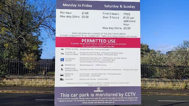 Sign for Mark Street Car Park detailing parking fees, hours, and conditions, with a yellow barrier in the foreground.