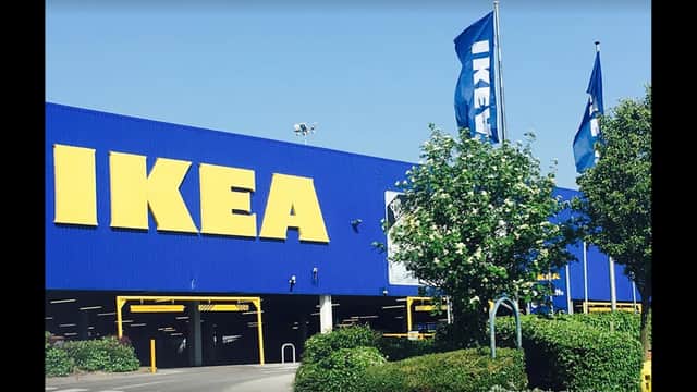 Bright blue IKEA building with large yellow signage, surrounded by green shrubs and flags waving in the breeze.