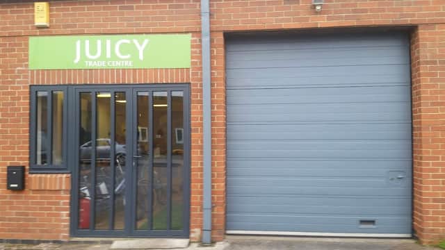 Green brick building with a green sign reading "JUICY TRADE CENTRE" and a gray garage door.