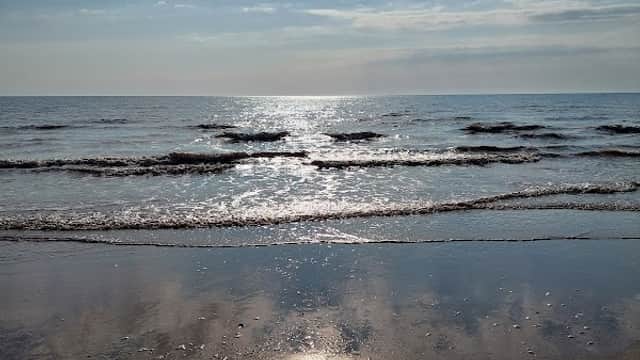 Sunlight reflects on calm waves at Barmston Beach, with a clear blue sky and scattered clouds above.