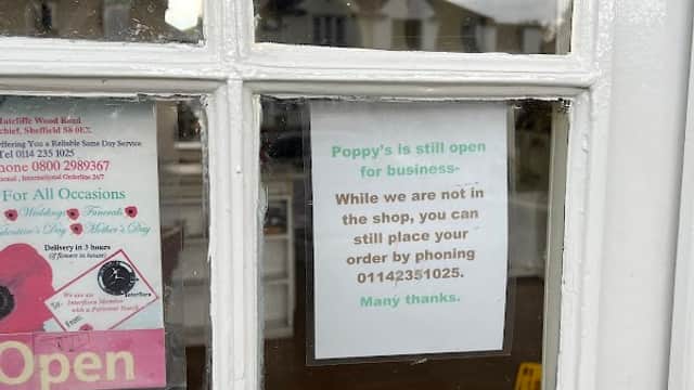 "Window of Poppy's Florist with a sign stating it's open for business and a phone number for orders."