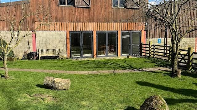 Rustic hotel building with wooden exterior, large windows, and grassy area featuring logs and trees in Low Row, Yorkshire.