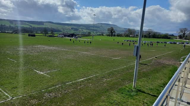 A rugby field with players in action, surrounded by hills and a clear blue sky in Leyburn, Yorkshire.