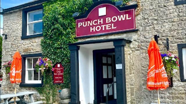 Historic stone building with a sign reading "Punch Bowl Hotel," surrounded by greenery and outdoor seating.
