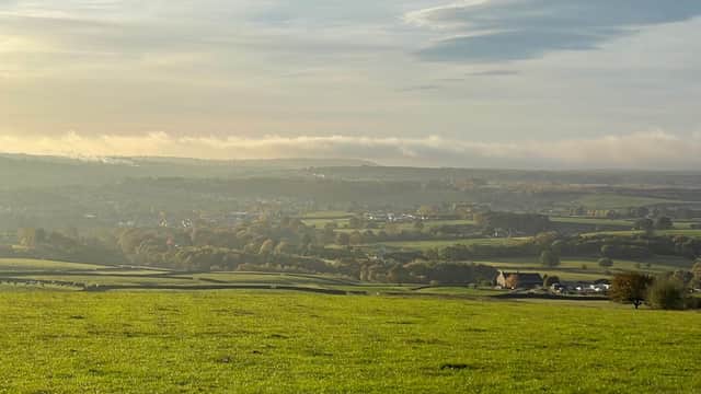 A panoramic view of rolling green hills and valleys under a cloudy sky, with distant villages and trees in the landscape.