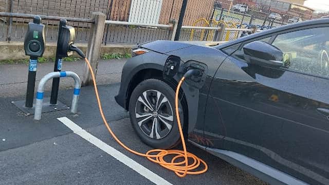 Connected Kerb charging station with an electric vehicle plugged in, orange charging cable visible, in a parking area.