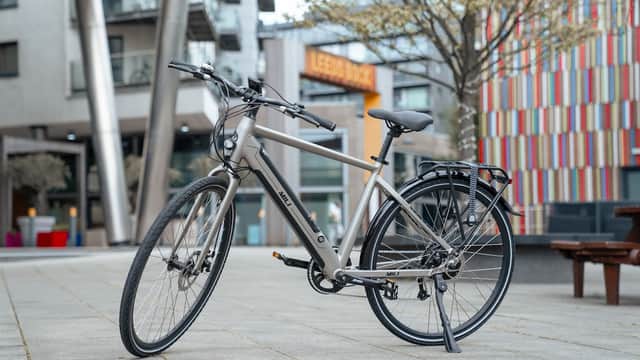A sleek gray bike parked on a paved area with modern buildings and colorful facades in the background.