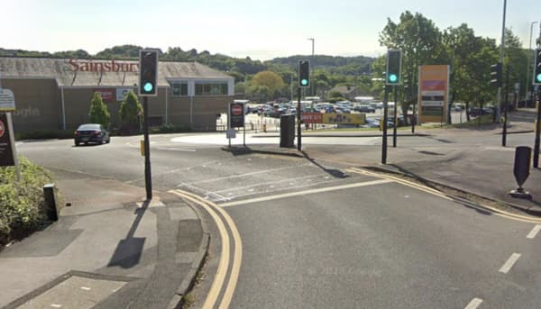 Busy roundabout with traffic lights, Sainsbury's store in the background, and multiple parked cars visible.